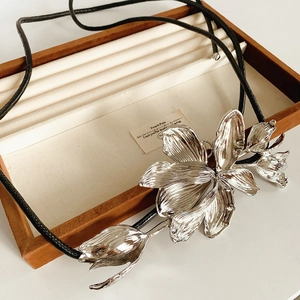 Macro view of silver tulip flower pendant with leather cord on a beige velvet tray