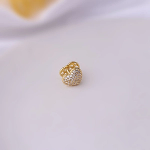 Golden heart-shaped copper earring with white zircon inlay on white fabric background