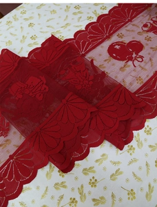 Detailed embroidery of Christmas bells on red lace table runner with tassels