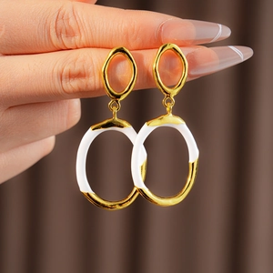 Close-up of model wearing gold and white enamel oval earrings in a minimalist style