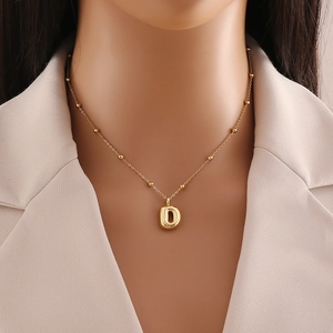 Close-up of golden letter D pendant with beaded chain worn on woman's neck