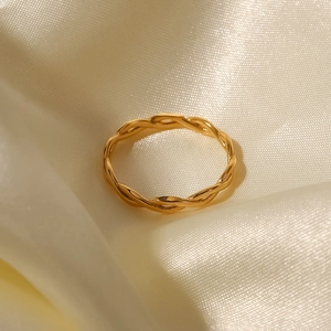 Close-up of a 18K gold plated twisted steel ring on an elegant beige silk fabric