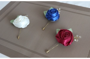 Close-up of handmade satin rose boutonnieres in white, blue and burgundy with gold pins