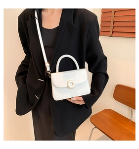 White glossy shoulder bag with gold circular buckle worn by model in black blazer