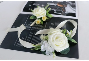 Detail of white foam rose corsage and wristlet set with cream satin ribbon and greenery
