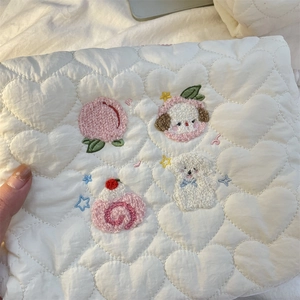 Detailed view of cream quilted makeup bag featuring embroidered cartoon motifs and heart pattern