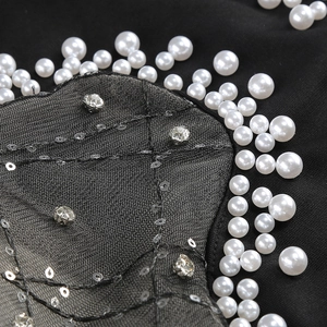 Close-up of white pearls, silver sequins and rhinestones on black mesh dress fabric