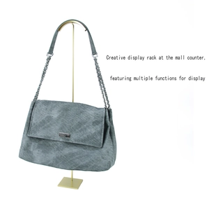 Detail of grey suede chain bag hanging on a gold metal handbag display stand