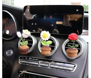 Three handmade crochet flower car air vent clips installed on a luxury vehicle dashboard