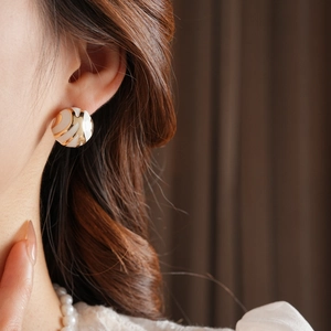 Close-up of white enamel and gold spherical earrings worn on a female model's ear