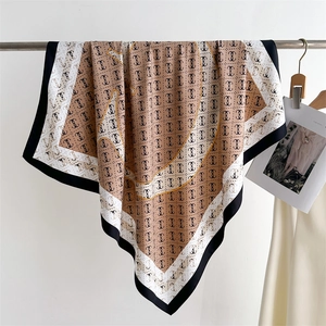 Silk-like square scarf with brown letter monogram pattern hanging on a metal hanger