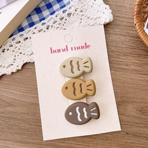 Detailed view of three cute fish-shaped hair clips in beige and brown on card packaging