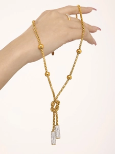 Detail of long gold chain necklace with knot design and zircon encrusted pendants