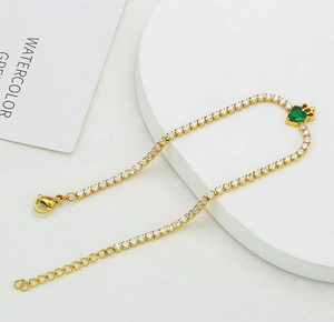 Detail of gold tennis bracelet with white zircon and green heart crown pendant