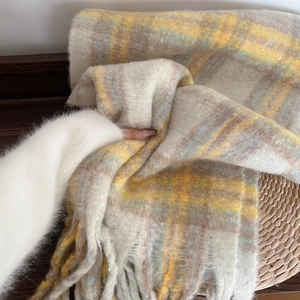 Close-up of soft beige plaid scarf with yellow and blue tassels on wooden background
