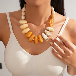Detail of chunky acrylic necklace with amber beads and gold spacers on a model