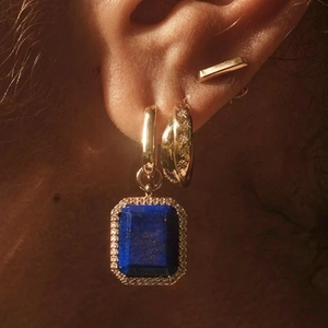 Close-up of gold star earrings with blue gemstone pendant and crystals on ear