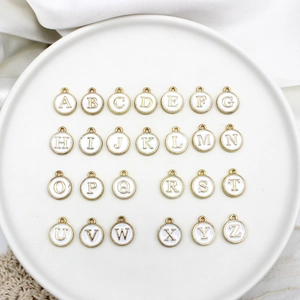 Macro detail of 26 round white enamel and gold alloy alphabet charms in a white tray