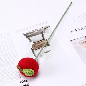 Detailed view of a handmade crochet red apple flower with a green stem on a white background