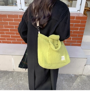Green plush shearling tote bag shown on model's shoulder against a brick wall background