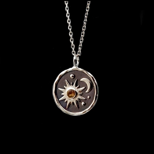Macro detail of sun and moon pendant necklace with yellow gemstone and silver finish