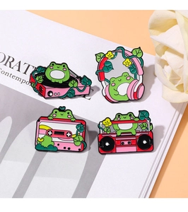 Close-up of four cute cartoon frog music enamel pins featuring record players and tapes