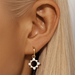 Close-up of gold opal sunburst earring featuring white stones on ear model