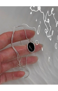 Macro detail of silver necklace with oval black onyx pendant held over rippling water