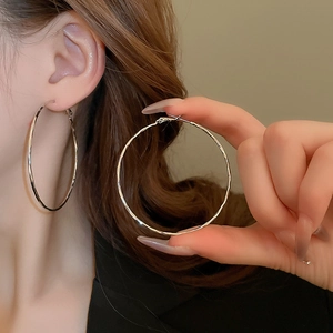 Macro shot of large silver geometric hoop earrings with subtle hammered metal texture
