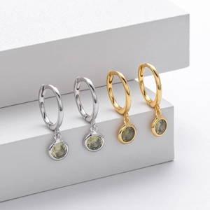 Detail of silver and gold hoops featuring round light green gemstone pendants on white stands