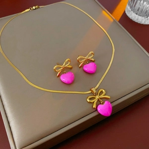 Vue détaillée de l'ensemble collier nœud doré et boucles d'oreilles cœur rose fuchsia