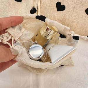 Detail view of champagne drawstring bag with black hearts holding luxury skincare products