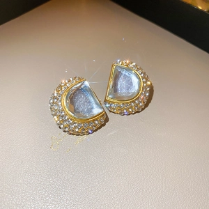 Close-up of D-shaped gold earrings with diamonds and clear crystals on a jewelry box