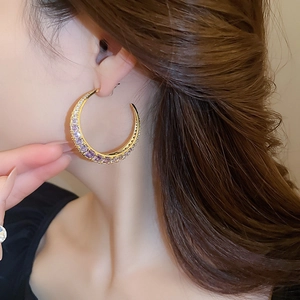 Close-up of a model wearing gold crescent earrings with purple and clear zircon stones