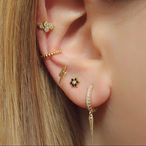 Detailed close-up of gold-plated spiked cone earrings and zircon studs worn by a model