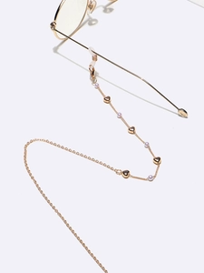Détail de la chaîne de lunettes dorée avec pendentifs en cœur et perles synthétiques
