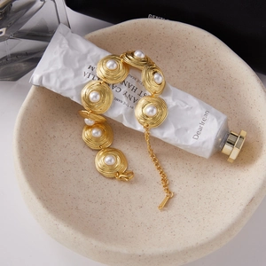 Detail showing vintage golden bracelet with pearl-inlaid rings on a beige display stand