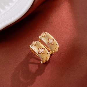 Detail of gold clover earrings with brushed texture and zircon accents on silk