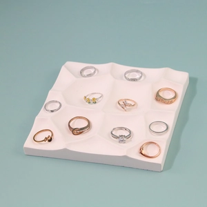 White geometric resin jewelry display tray with rings on light blue background