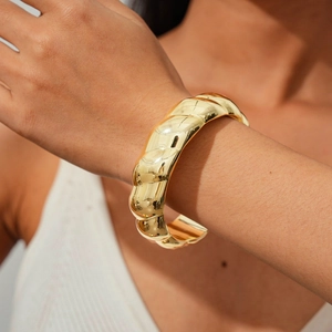 Detailed view of a thick gold-finish twisted cuff bracelet in irregular geometric metal style