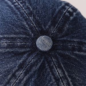 Detailed macro view of the dark blue denim texture and button on the baseball cap
