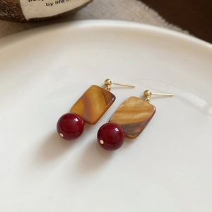 Detail of square shell earrings with red beads on a white ceramic plate