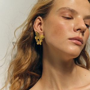Detailed close-up of golden butterfly earrings with brushed metal texture on female model