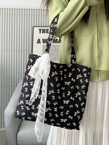 Detail of black canvas tote bag with gold bow print and long white lace ribbons