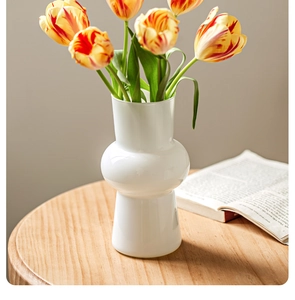Detail of white ceramic double-sphere vase featuring fresh orange tulips on a wooden desk
