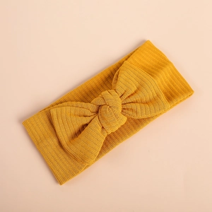 Soft yellow knitted baby headband with a large bow on a flat pink background
