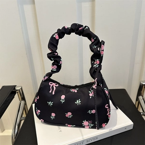 Chic black fabric shoulder bag with pink rose and bow prints on a white book