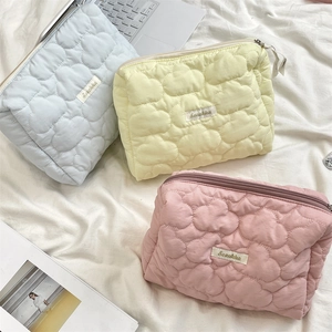 Three quilted makeup bags in blue, yellow, and pink on white bedding with accessories