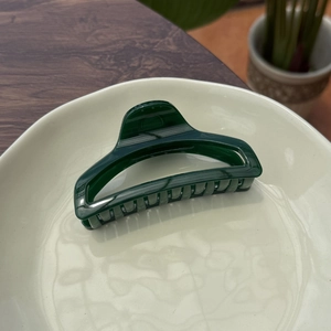 Detailed view of large dark green perfume bottle hair claw clip on a stylish cream tray