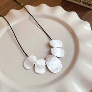 Detailed view of an irregular geometric white pendant on a black leather cord necklace